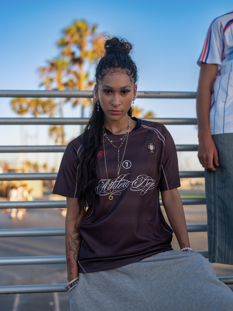 Maria Williams seated on a railing in a BLRD jersey with palm trees behind