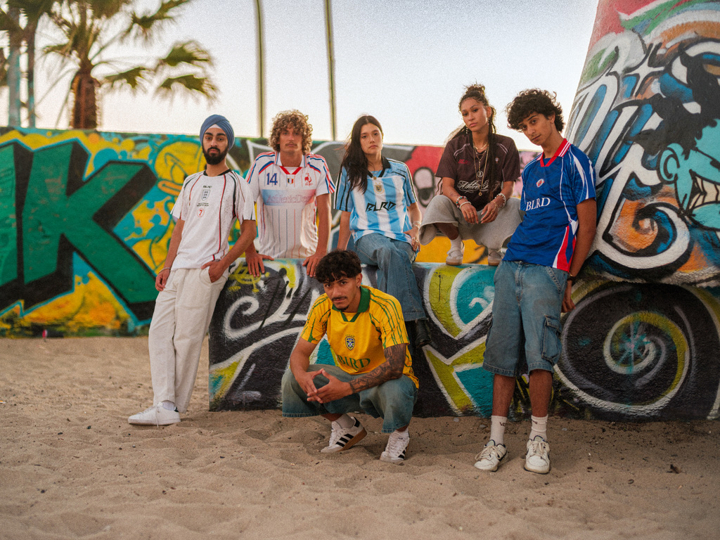 BLRD cast in soccer jerseys in front of a graffiti wall at the beach