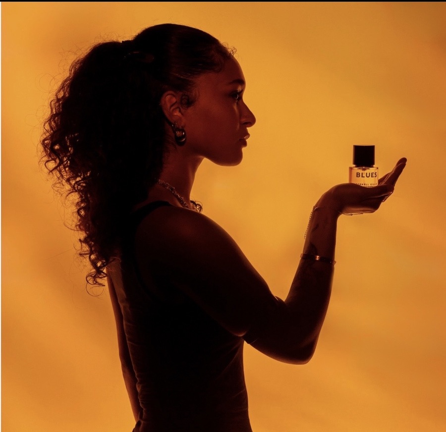 Maria Williams in silhouetted profile holding a bottle of Blues fragrance against a glowing amber backdrop