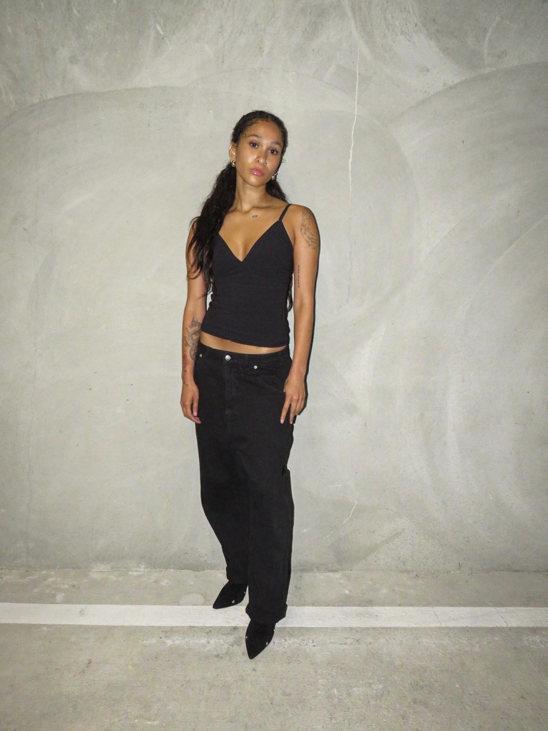 Digital — full-length front in black cami and black jeans against a concrete wall