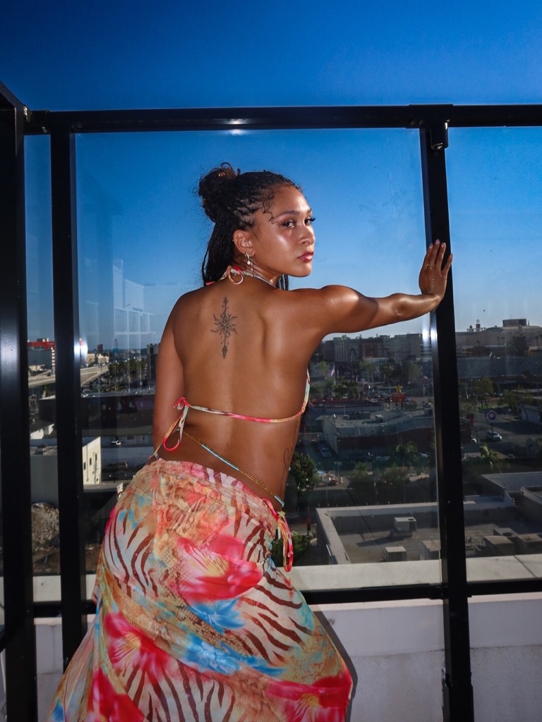 Maria Williams looking back over her shoulder against a rooftop glass railing above the city