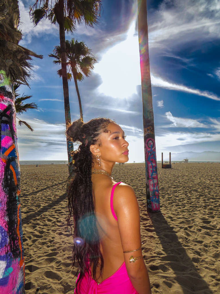 Maria Williams in profile on the sand with sun flare between palm trees