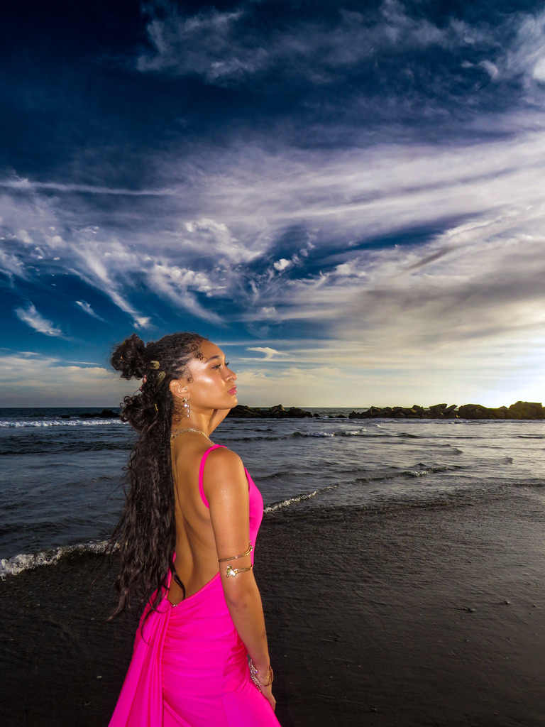 Close profile of Maria Williams in a backless pink gown at the water under a dramatic sky